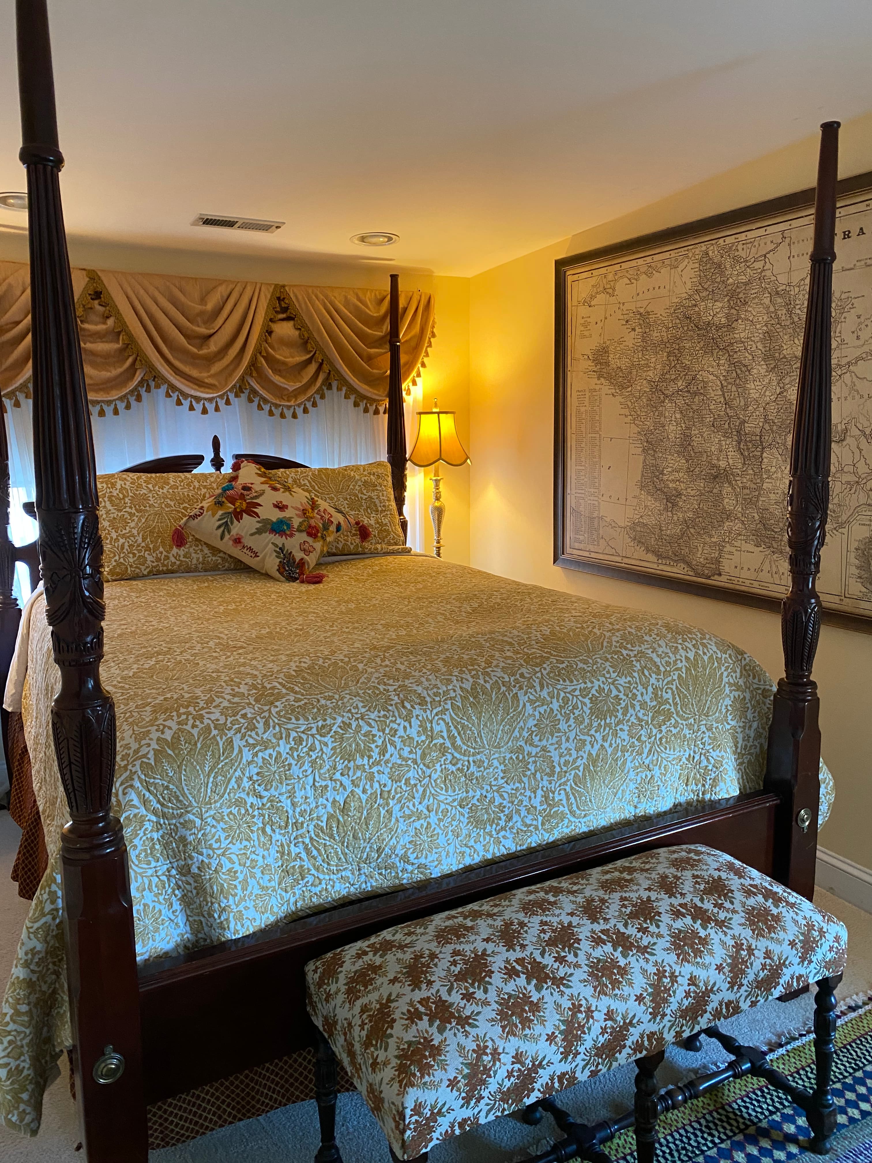 A cozy bedroom featuring a four-poster bed with floral bedding and a matching upholstered bench.
