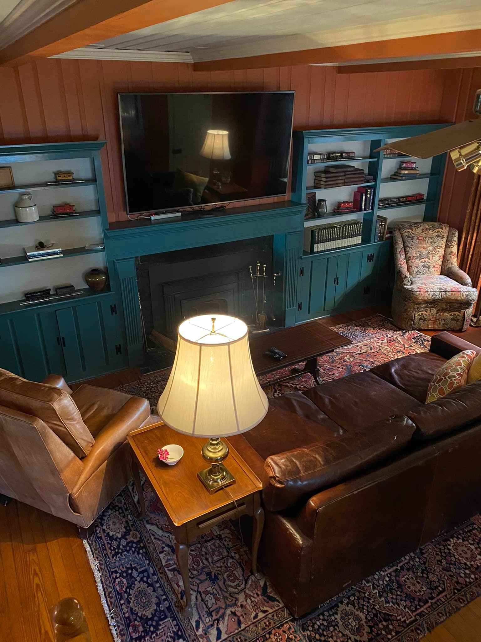 Cozy living room featuring a large TV, two armchairs, a sofa, and a table with a lamp on a patterned rug.
