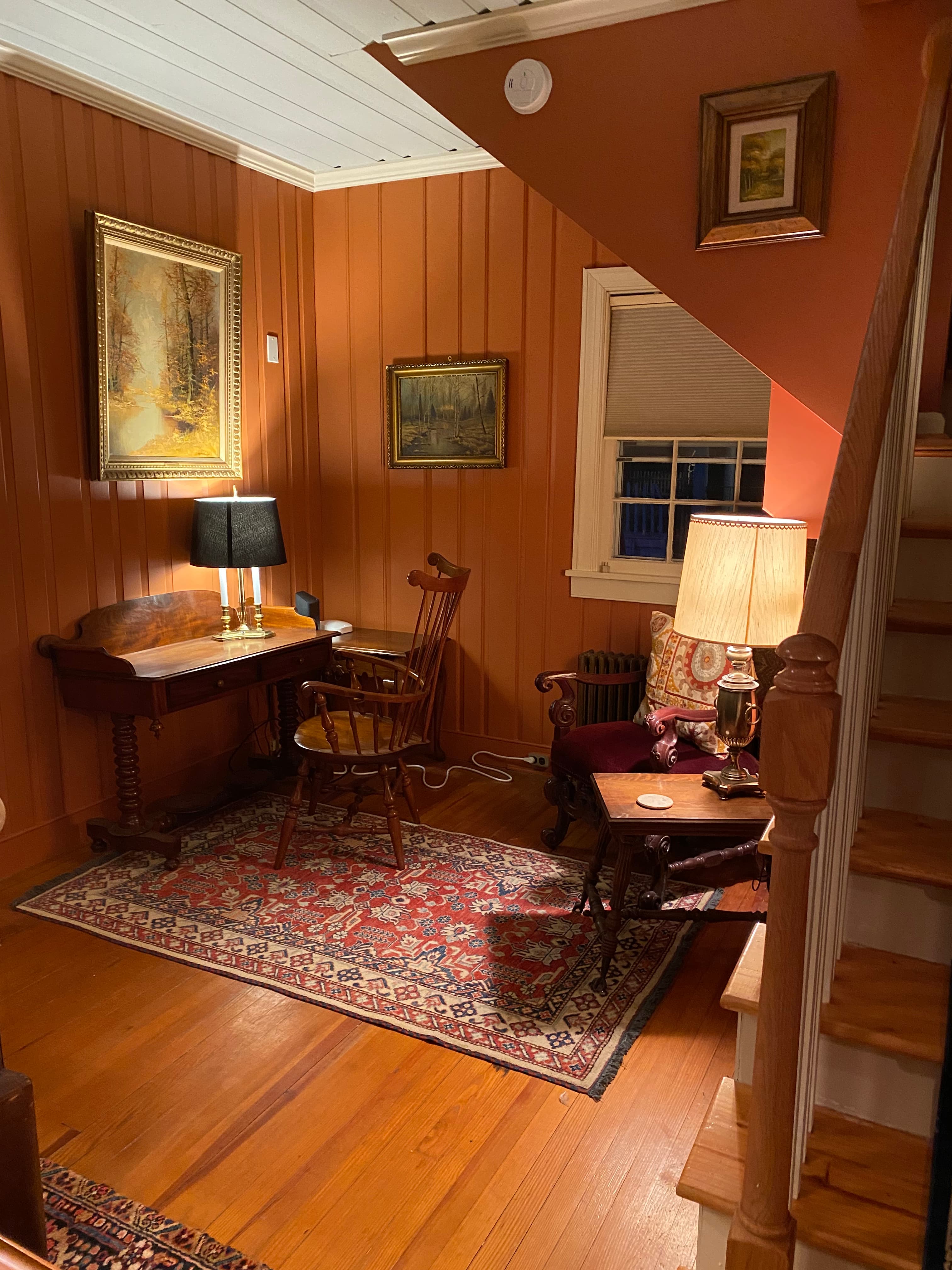 Cozy corner of a warmly decorated room featuring a wooden desk, a rocking chair, and warm lighting.