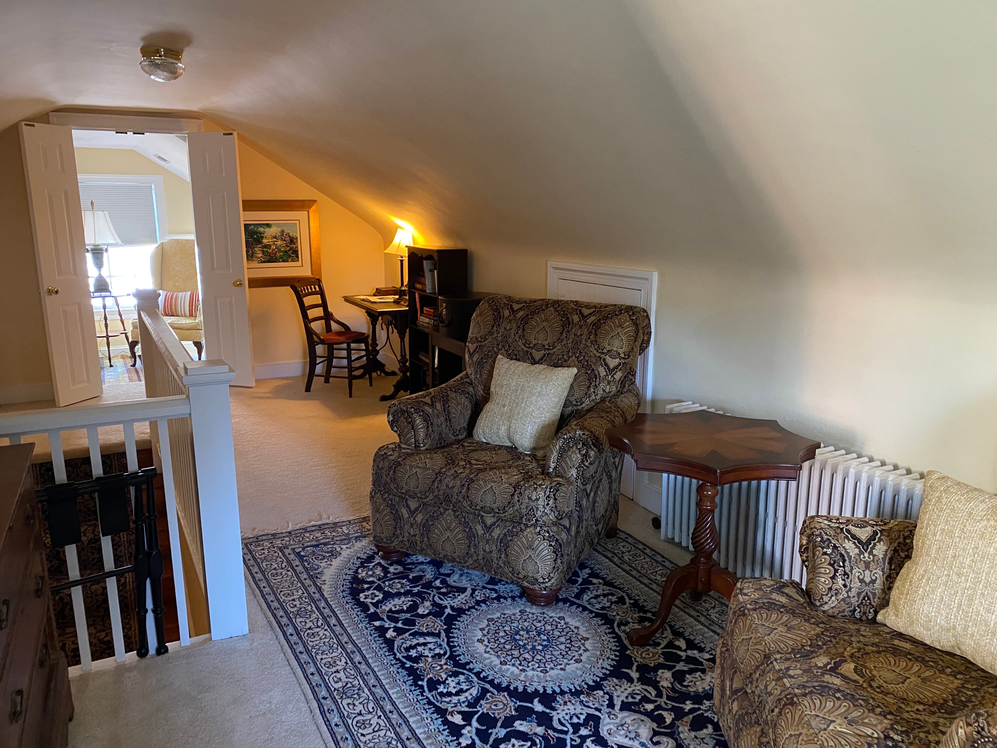 Cozy attic sitting area with plush chairs, a small table, and a view of an adjacent room.