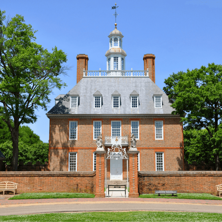 Historic brick building with a cupola, surrounded by trees and a garden.