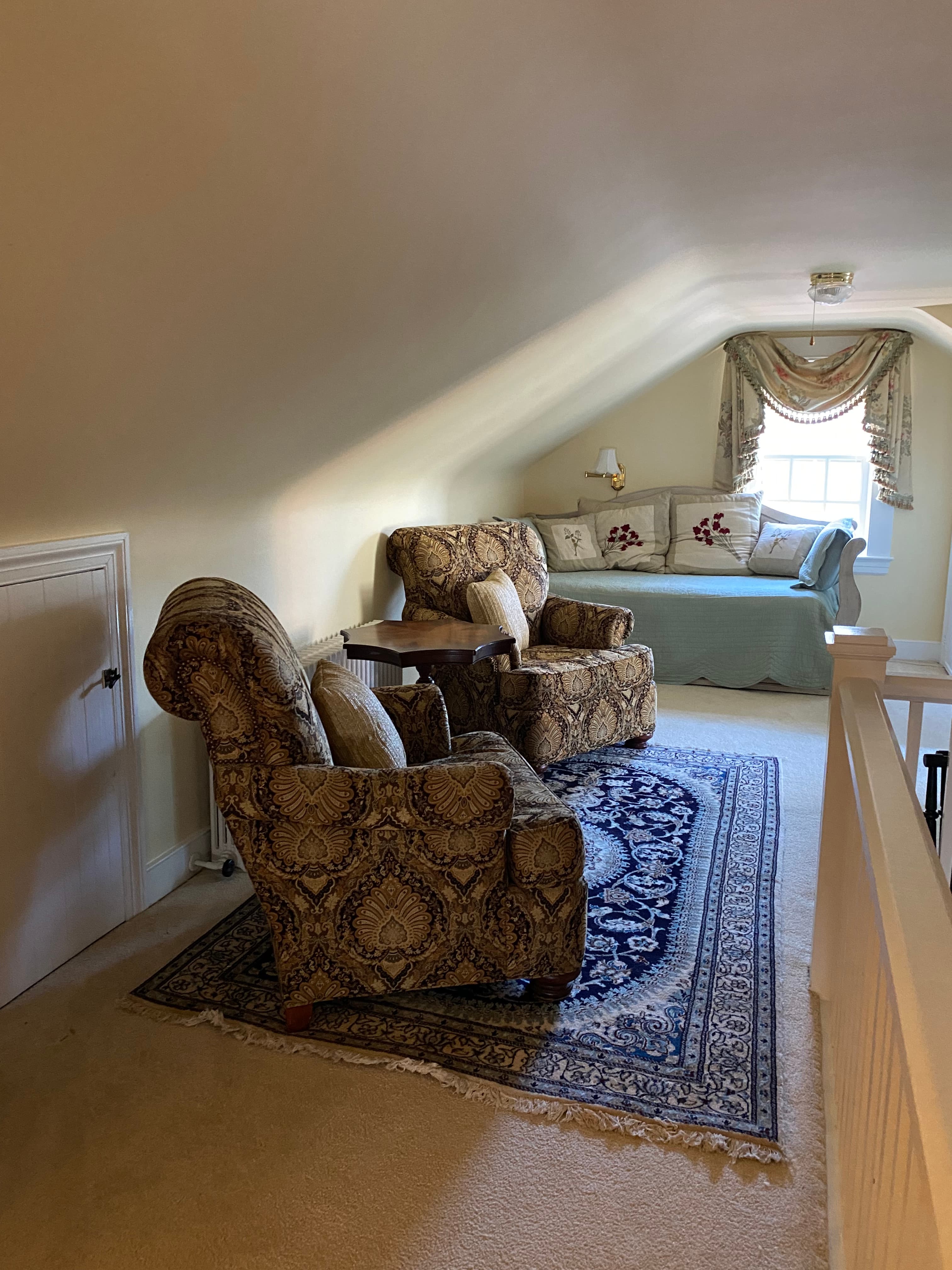 A cozy attic sitting area with plush armchairs, a small table, and a decorative window seat.