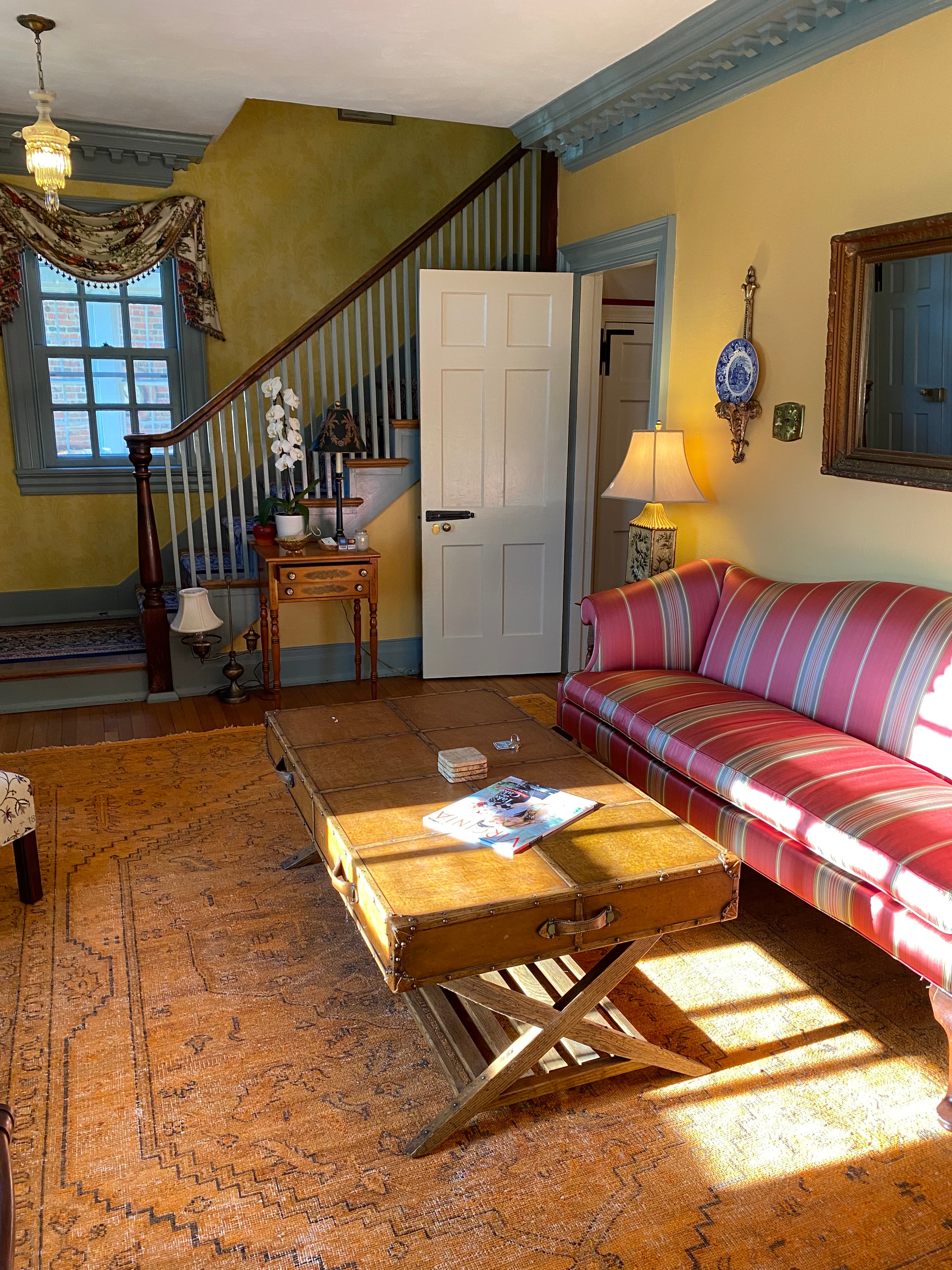 A cozy living room featuring a striped sofa, a wooden coffee table, and a staircase in the background.