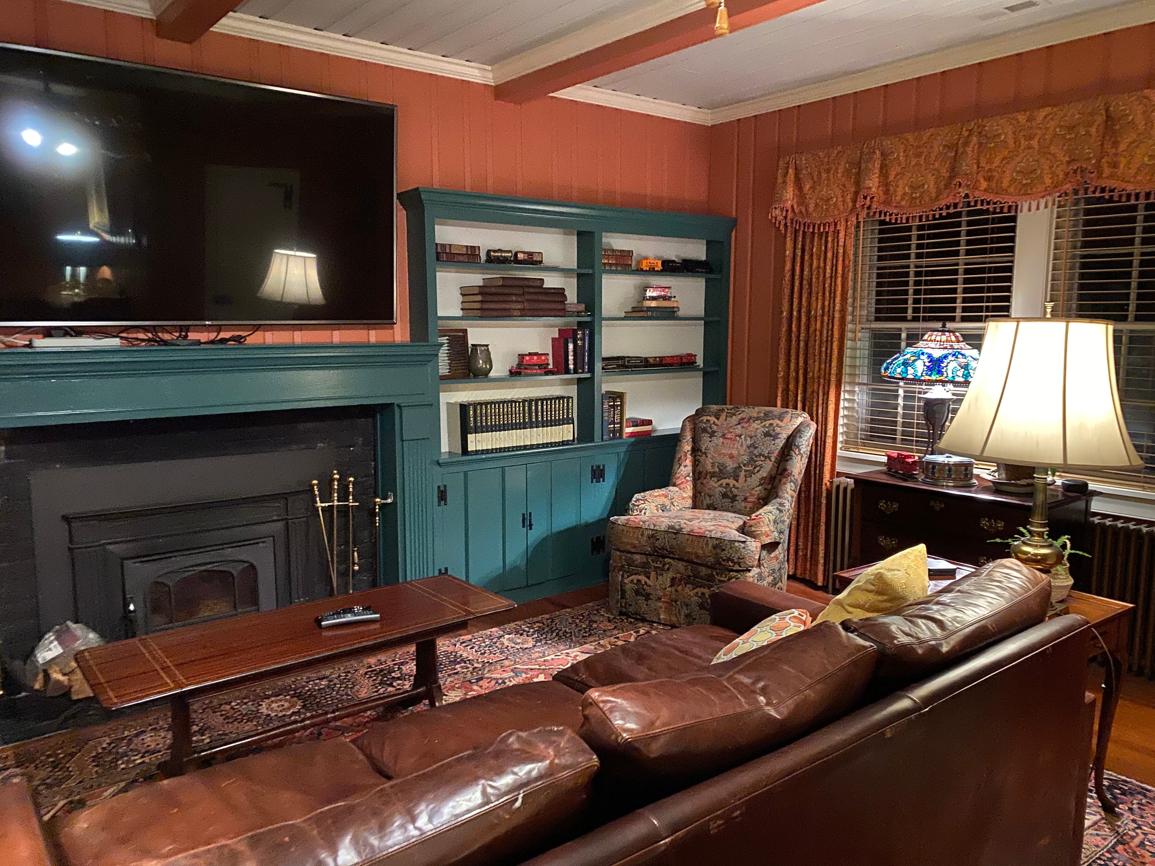 Cozy living room featuring a leather sofa, armchair, and a fireplace with a TV above a teal mantle.