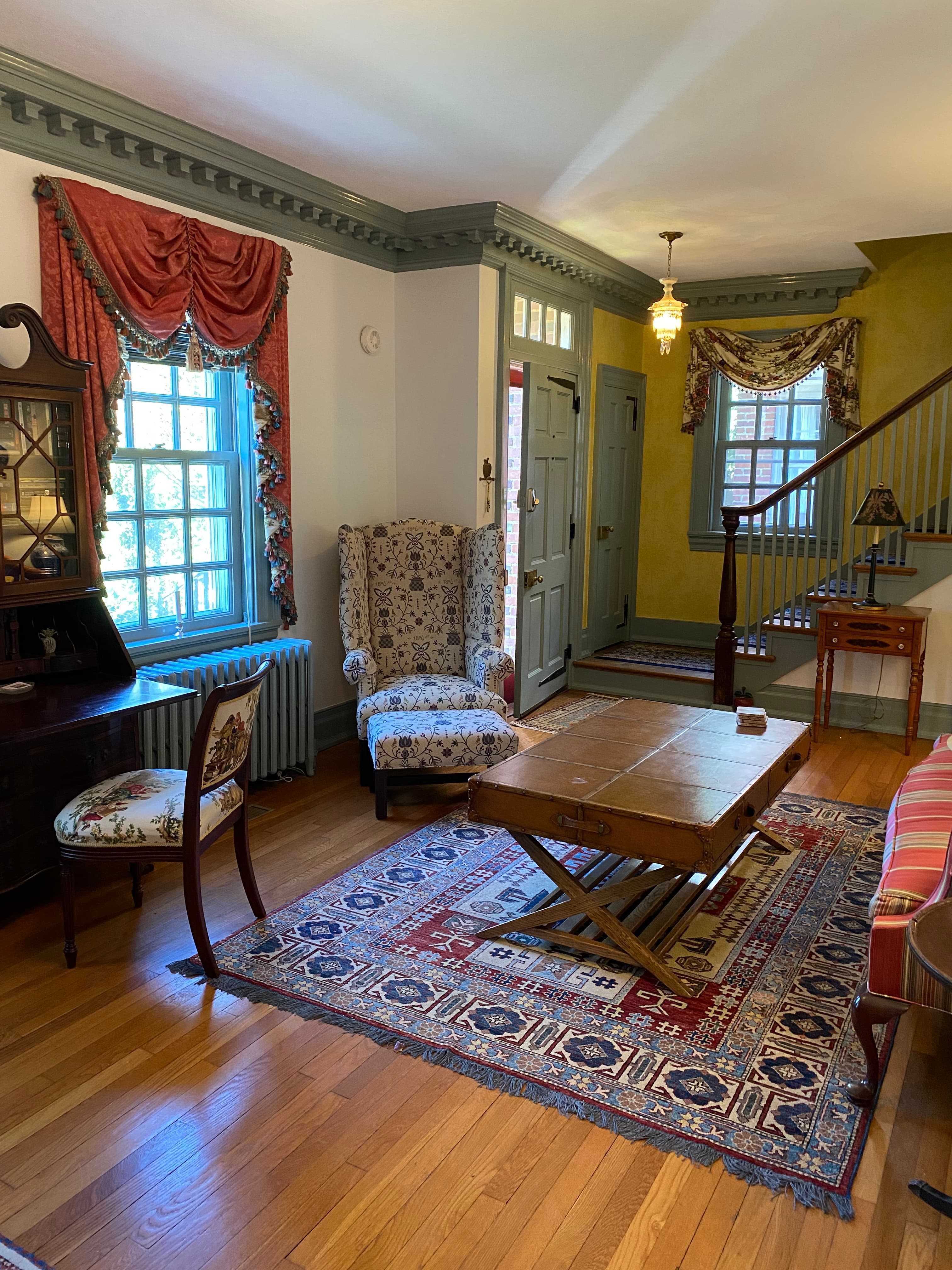 A cozy living room featuring patterned curtains, a wooden coffee table, and a staircase in the background.