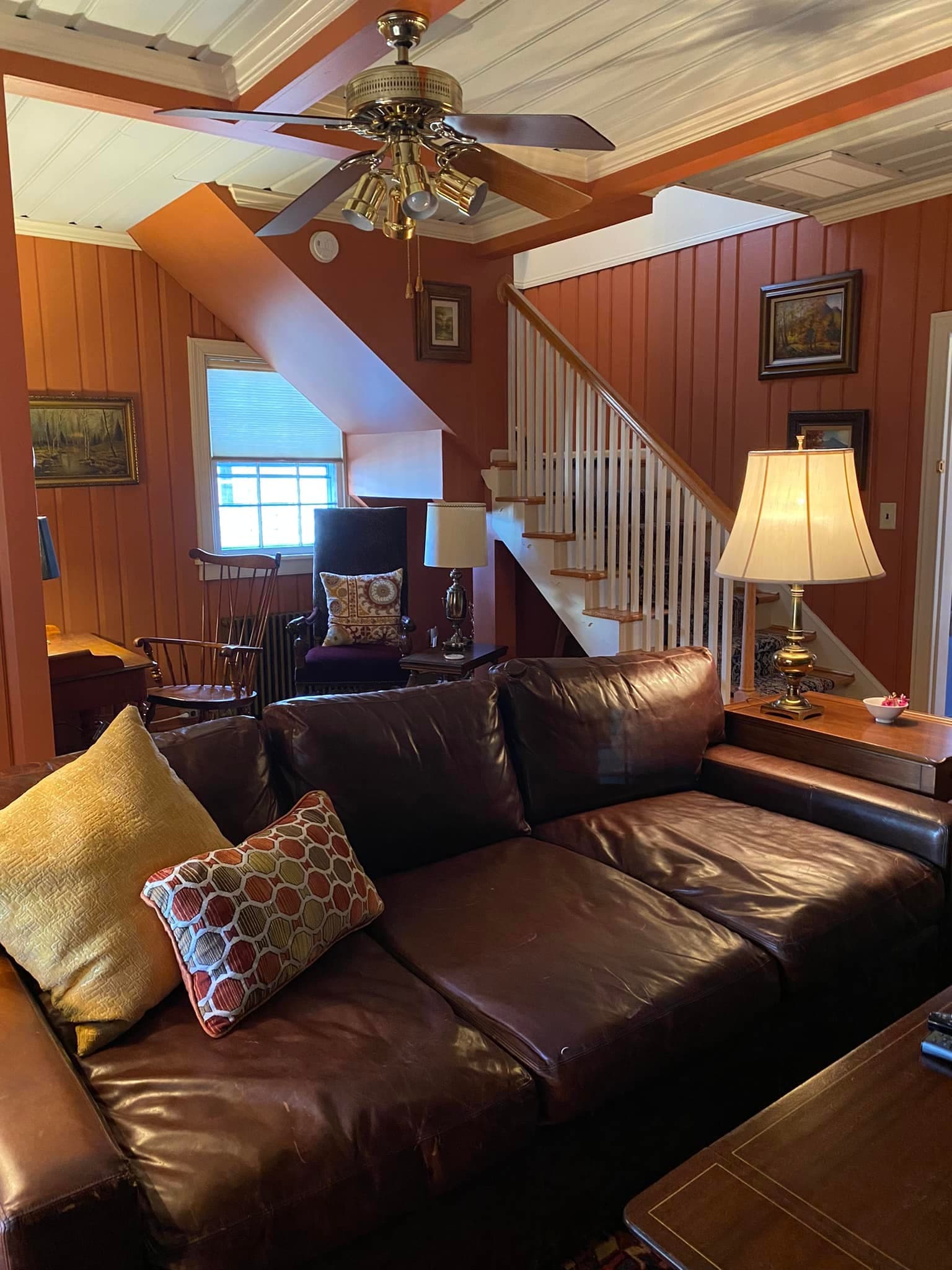 Cozy living room featuring a brown leather sofa, decorative pillows, a wooden staircase, and warm-toned walls.