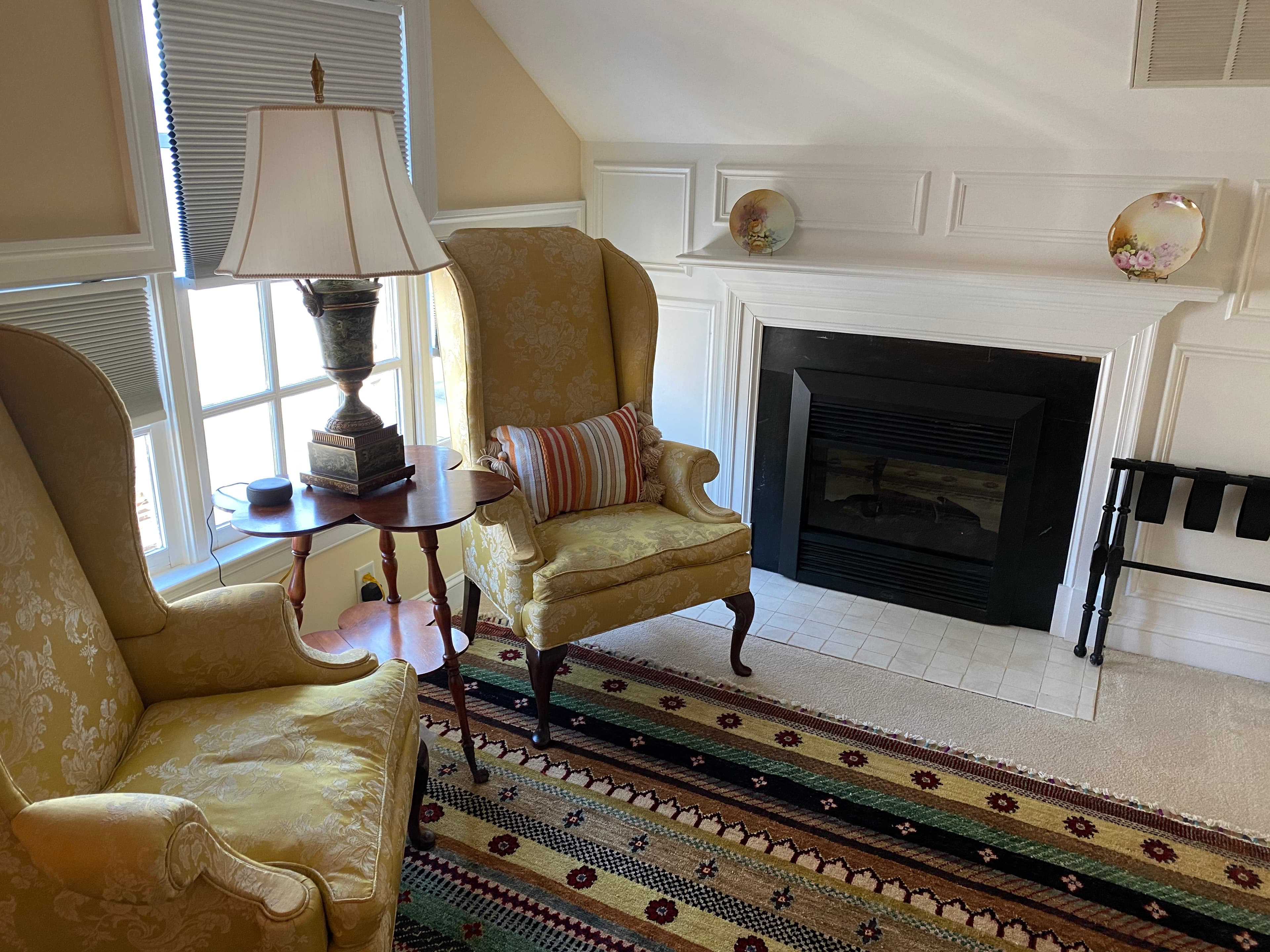 Cozy seating area with two yellow armchairs, a lamp, and a fireplace, complemented by a patterned rug.