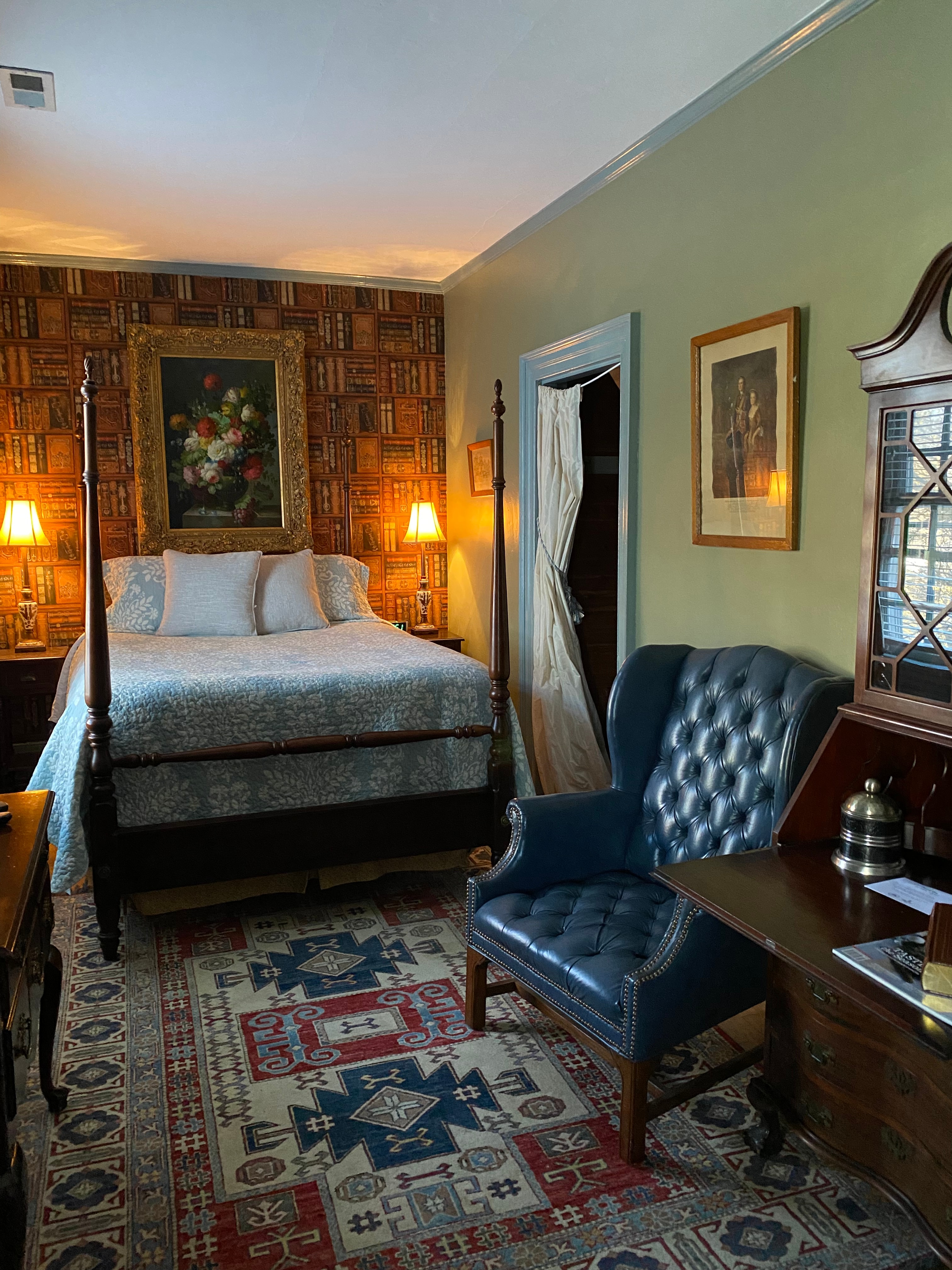 A cozy bedroom featuring a four-poster bed, vintage decor, and a blue armchair.