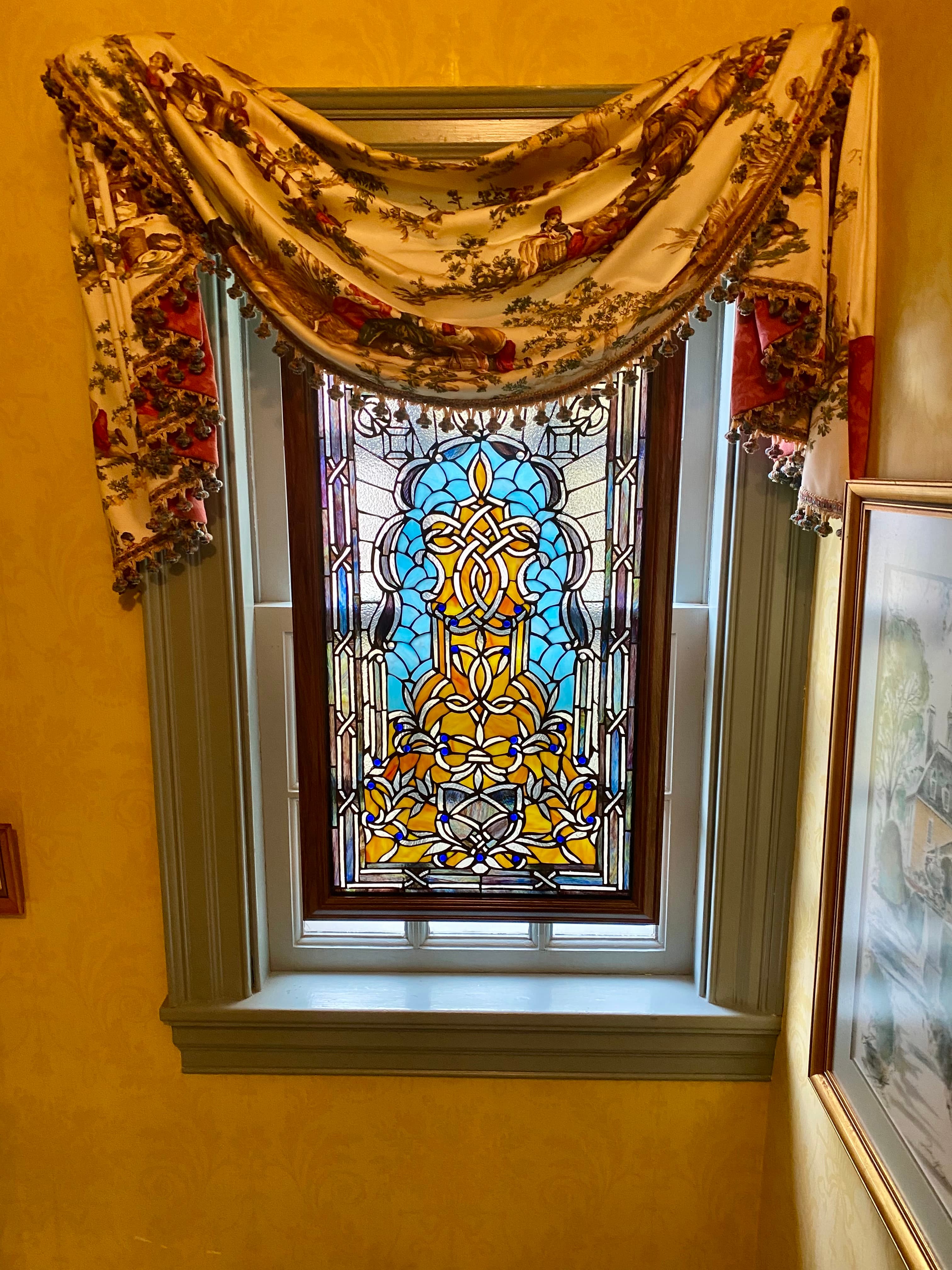 A stained glass window with intricate blue and yellow patterns, framed by decorative fabric drapery.