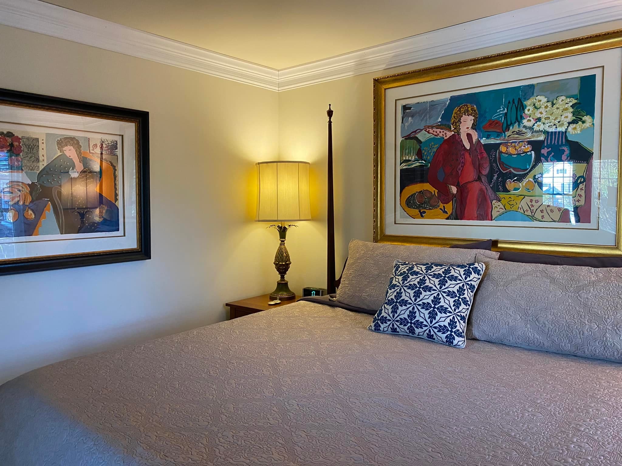A cozy bedroom featuring a large bed with a decorative pillow, a lamp on a nightstand, and two framed artworks on the walls.