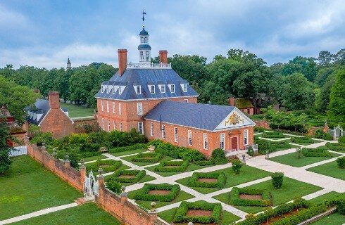 Aerial view of a colonial home and lush decorative garden area surrounded by trees