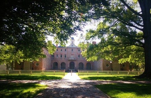 Front view of the exterior of an expansive brick building with lush green lawns and tall trees