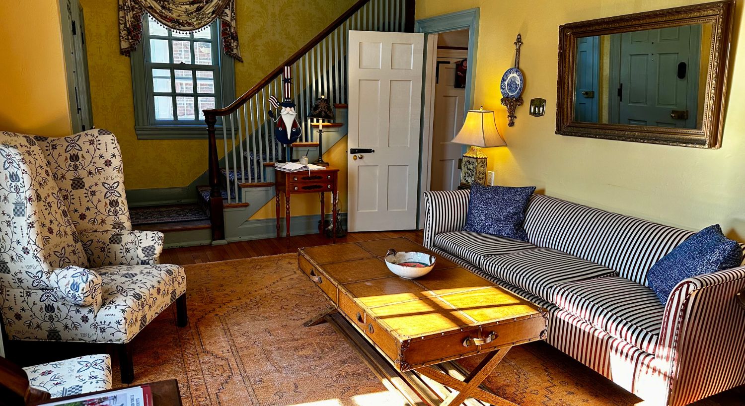 Living room with a striped couch, floral wingback chair, coffee table, decorative rug, stairway to an upper level