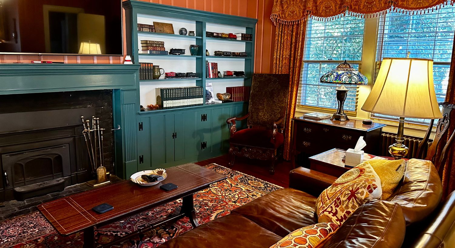 gallery-Living room with a brown leather couch, coffee table, decorative lamps in front of fireplace with TV above and built in bookshelves