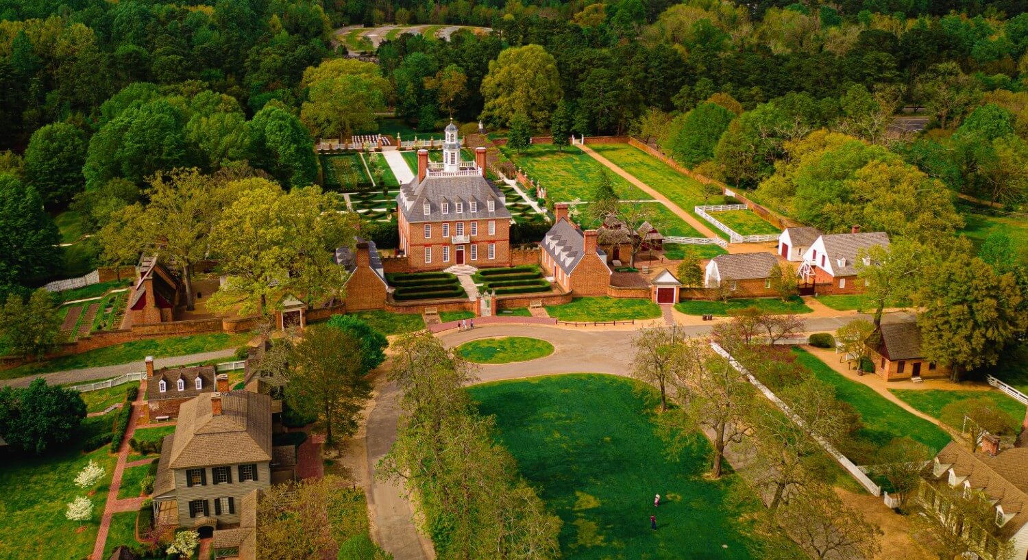 Aerial view of a colonial estate with decorative gardens and walkways, all surrounded by tall green trees