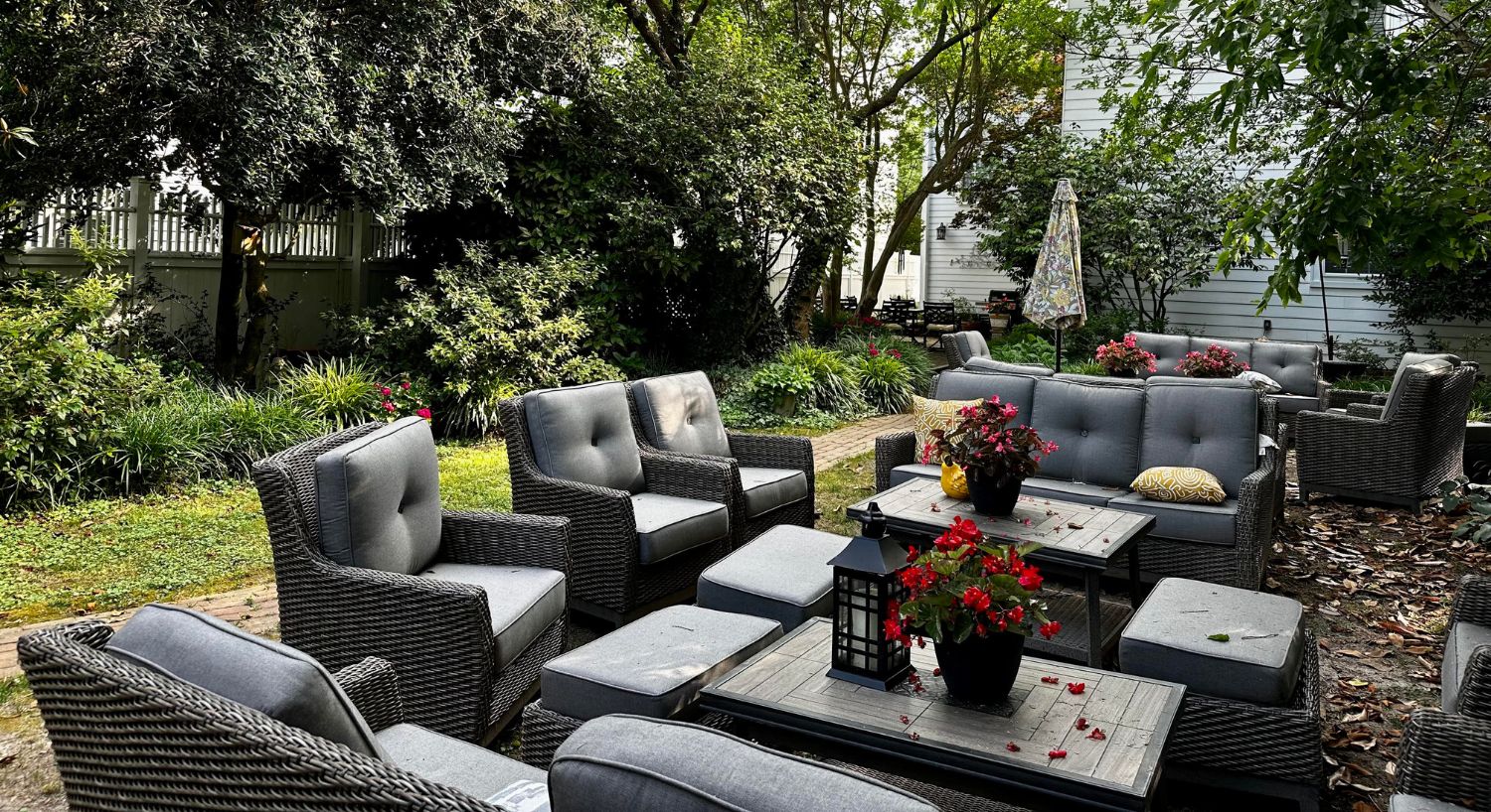 Backyard patio and garden area with multiple patio couches and chairs surrounded by lush plants and trees