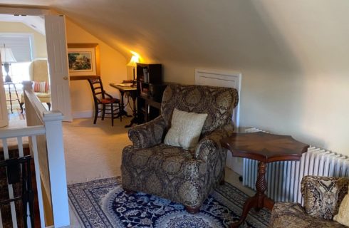 Sitting area with two plush sitting chairs, table, writing desk and doorway into a bedroom