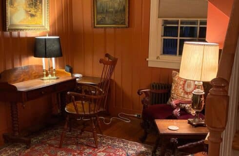 Corner of a living room with wood paneled walls, writing desk with a chair by a window