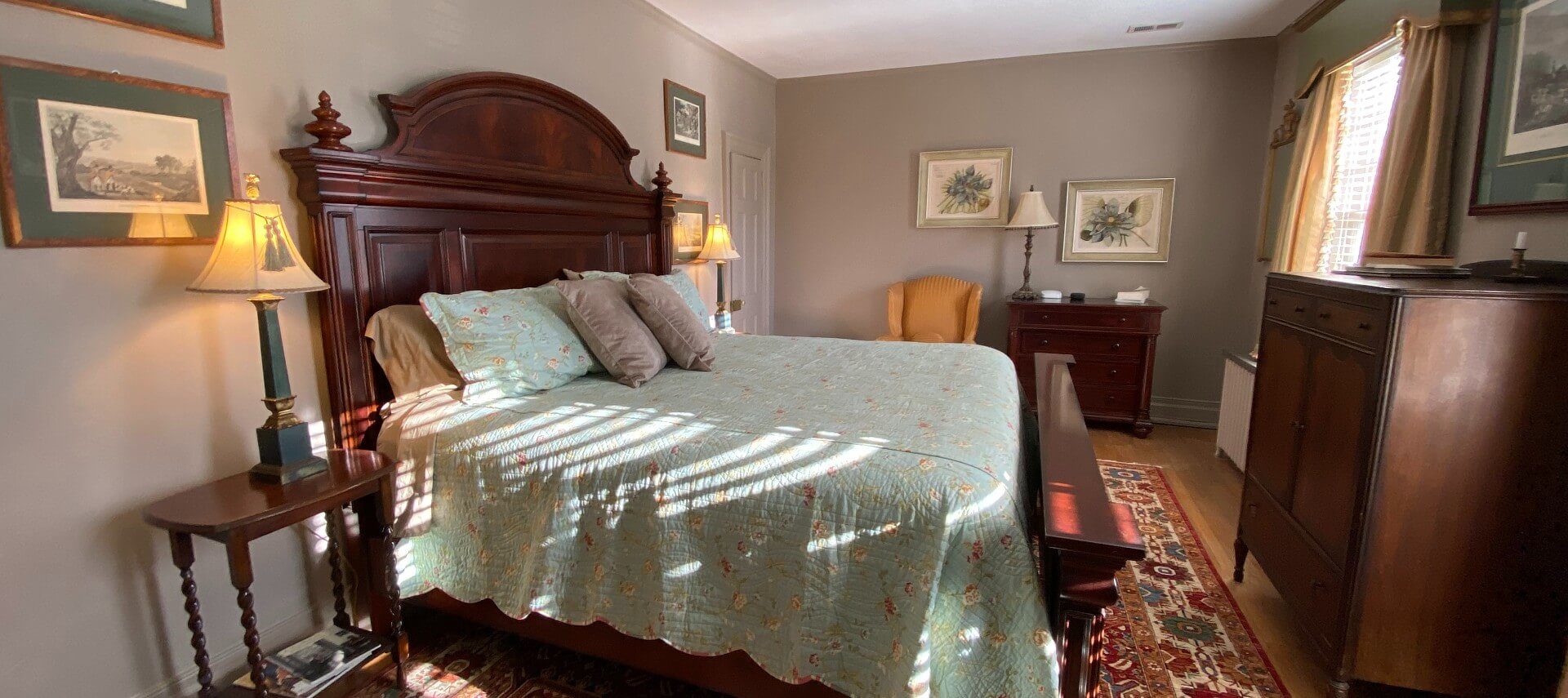 Beautiful spacious bedroom with king bed, mahogany headboard, side tables with lamps. decorative rug and hardwood floors