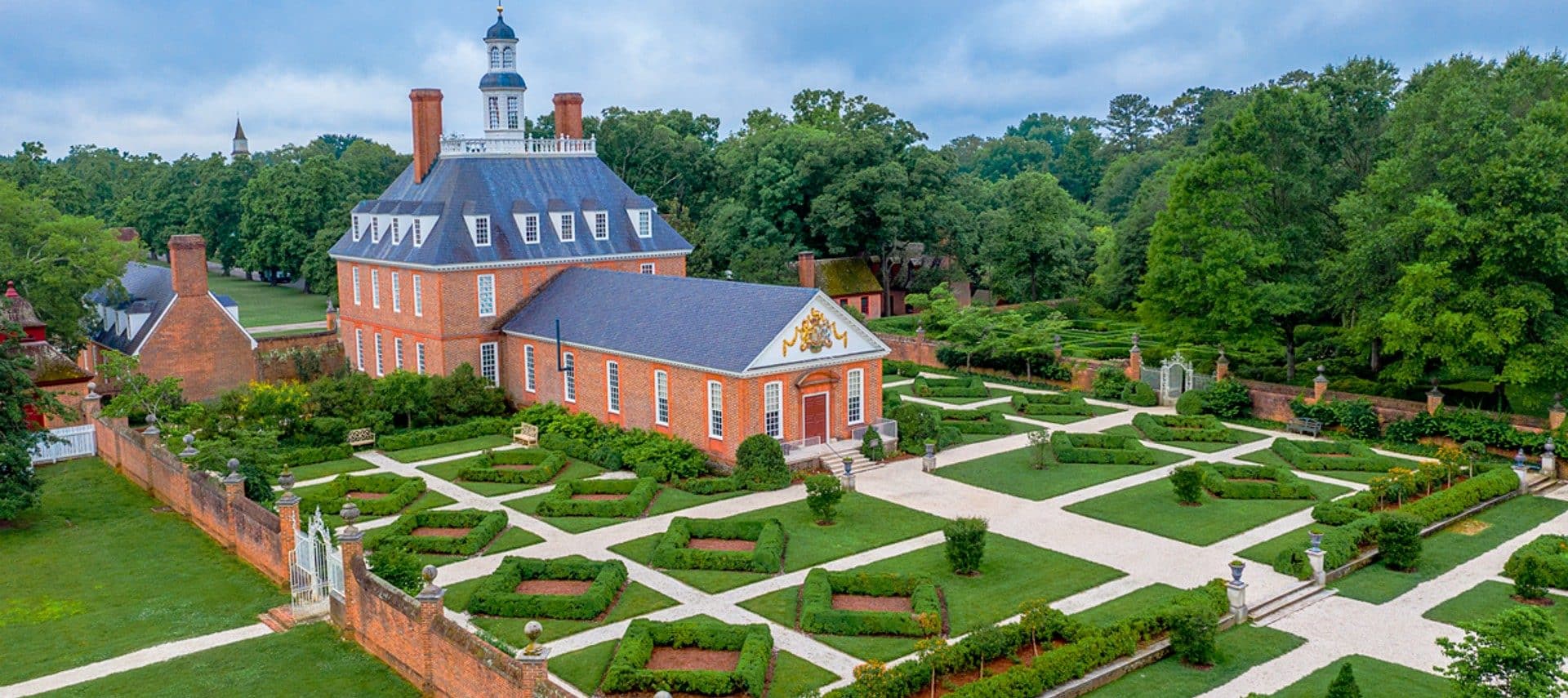 Aerial view of a colonial estate with decorative gardens and walkways, all surrounded by tall green trees