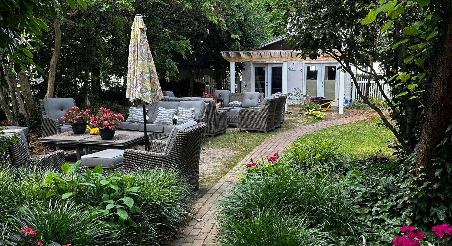 Backyard patio and garden area with multiple patio couches and chairs surrounded by lush plants and trees