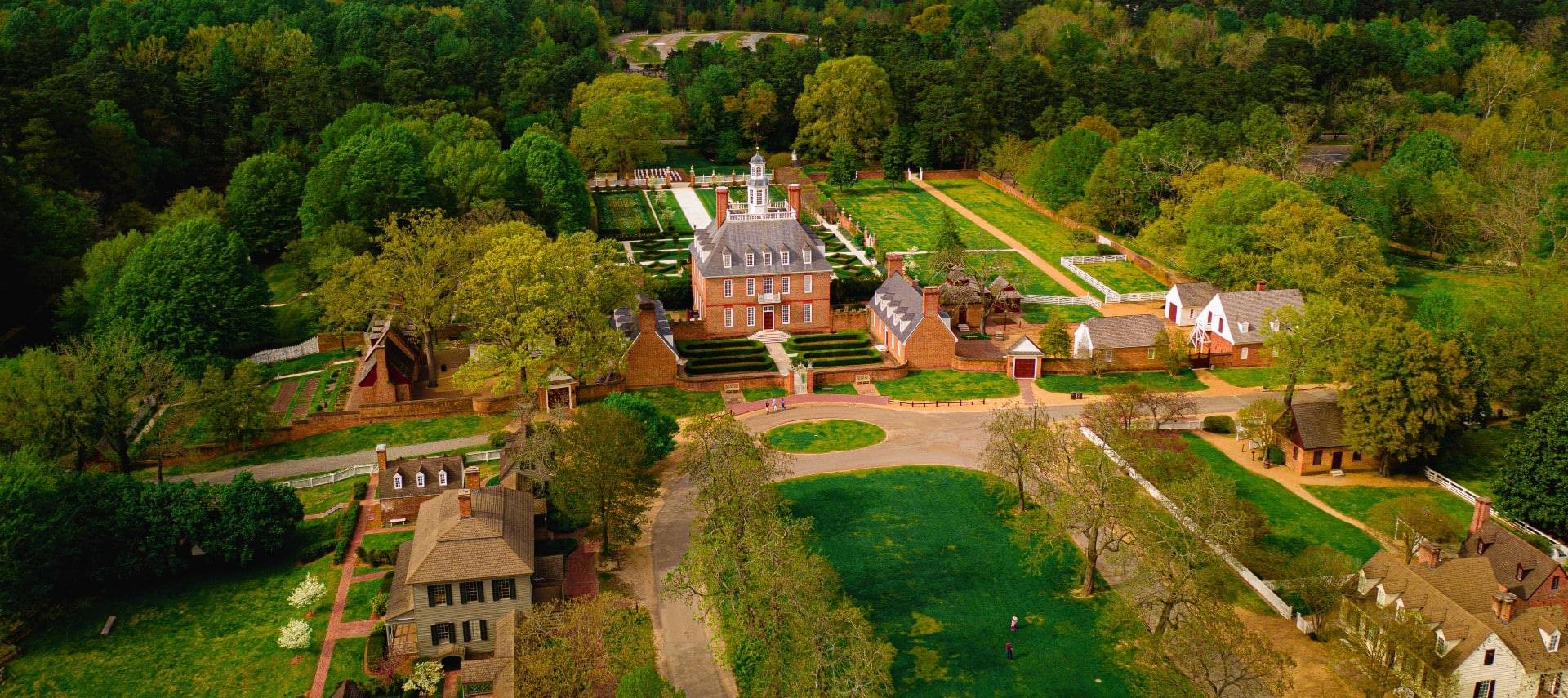 Aerial view of a large colonial estate with several homes, outbuildings and decorative lawns and gardens, all surrounded by dense forest of trees